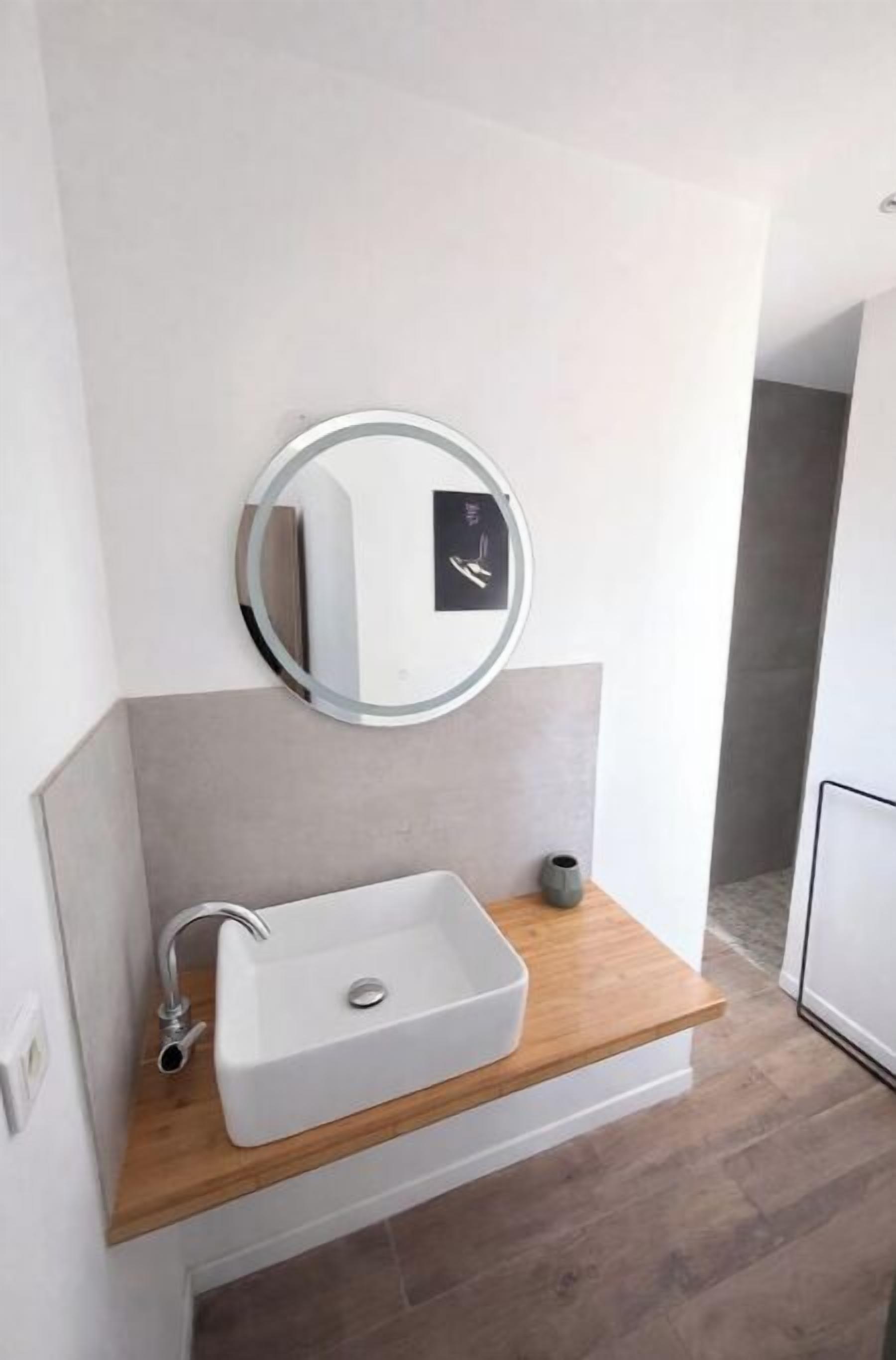 A modern bathroom with a white sink, a round mirror, and a wooden countertop.