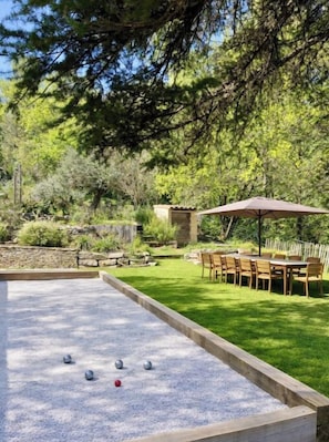 Une cour avec une table de jeu de palet, un coin repas avec des chaises et un parasol, et un mur en pierre.