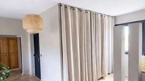 Un pasillo con una cortina color beige, una lámpara trenzada, una puerta de madera y un piso de baldosas.