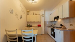 A kitchen with white cabinets, a dining table with chairs, a clock, and a stove. - Stella Cadente – Sea view retreat just steps from the beach (Golfo Aranci)