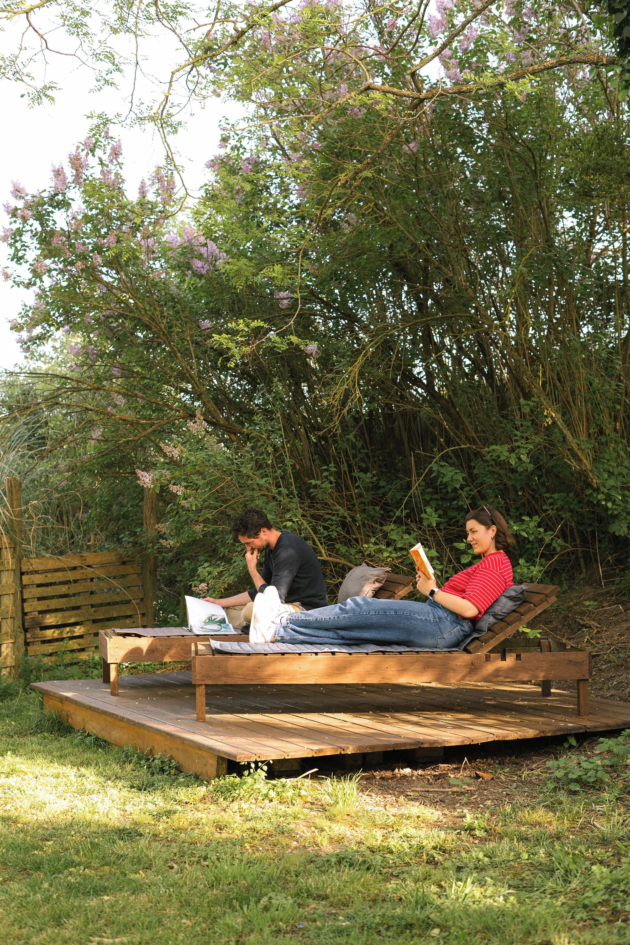Dos personas sentadas en un banco de madera en un jardín con árboles y una valla de madera.