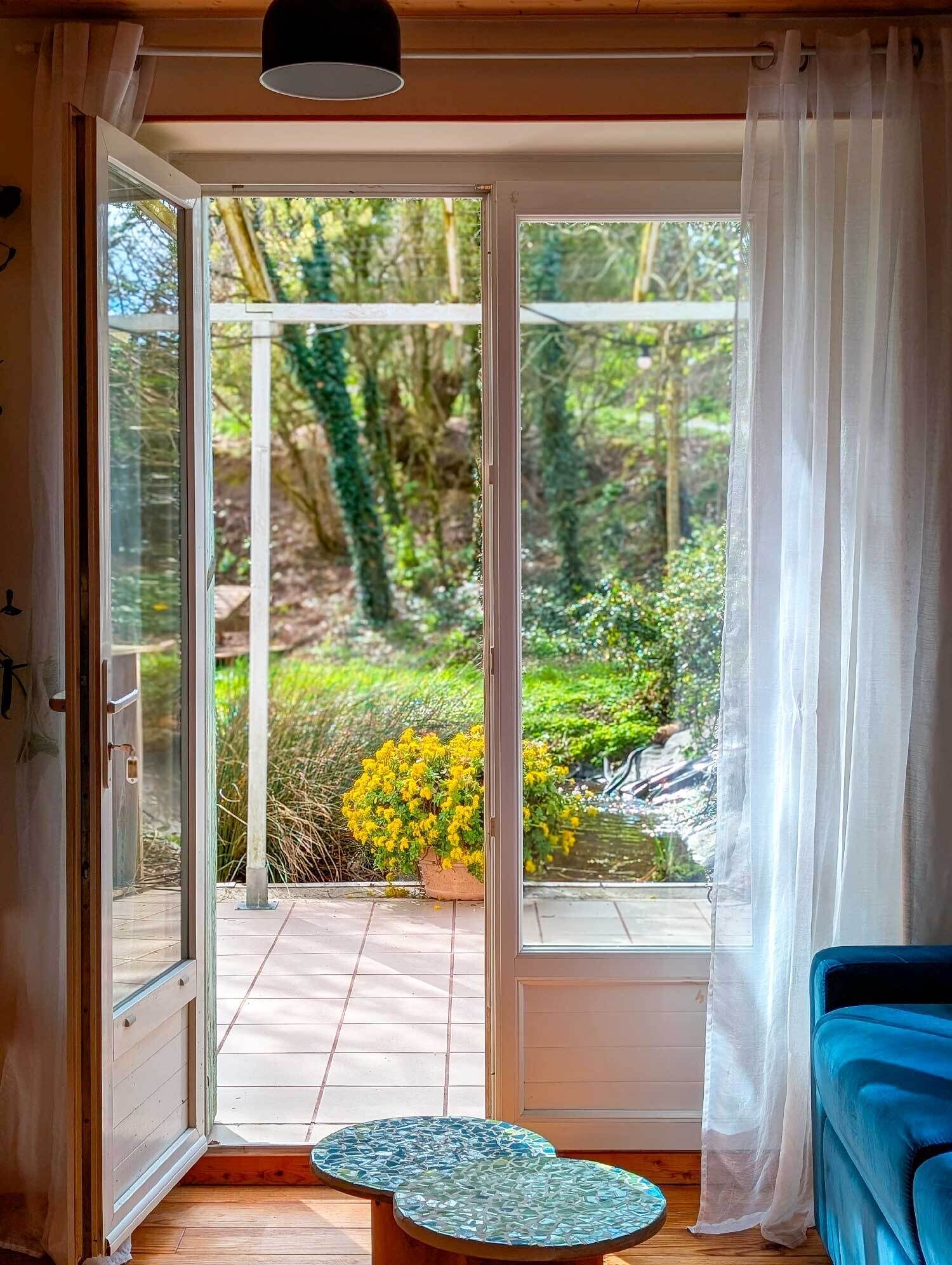 A room with a sliding glass door leading to a garden with yellow flowers and greenery.