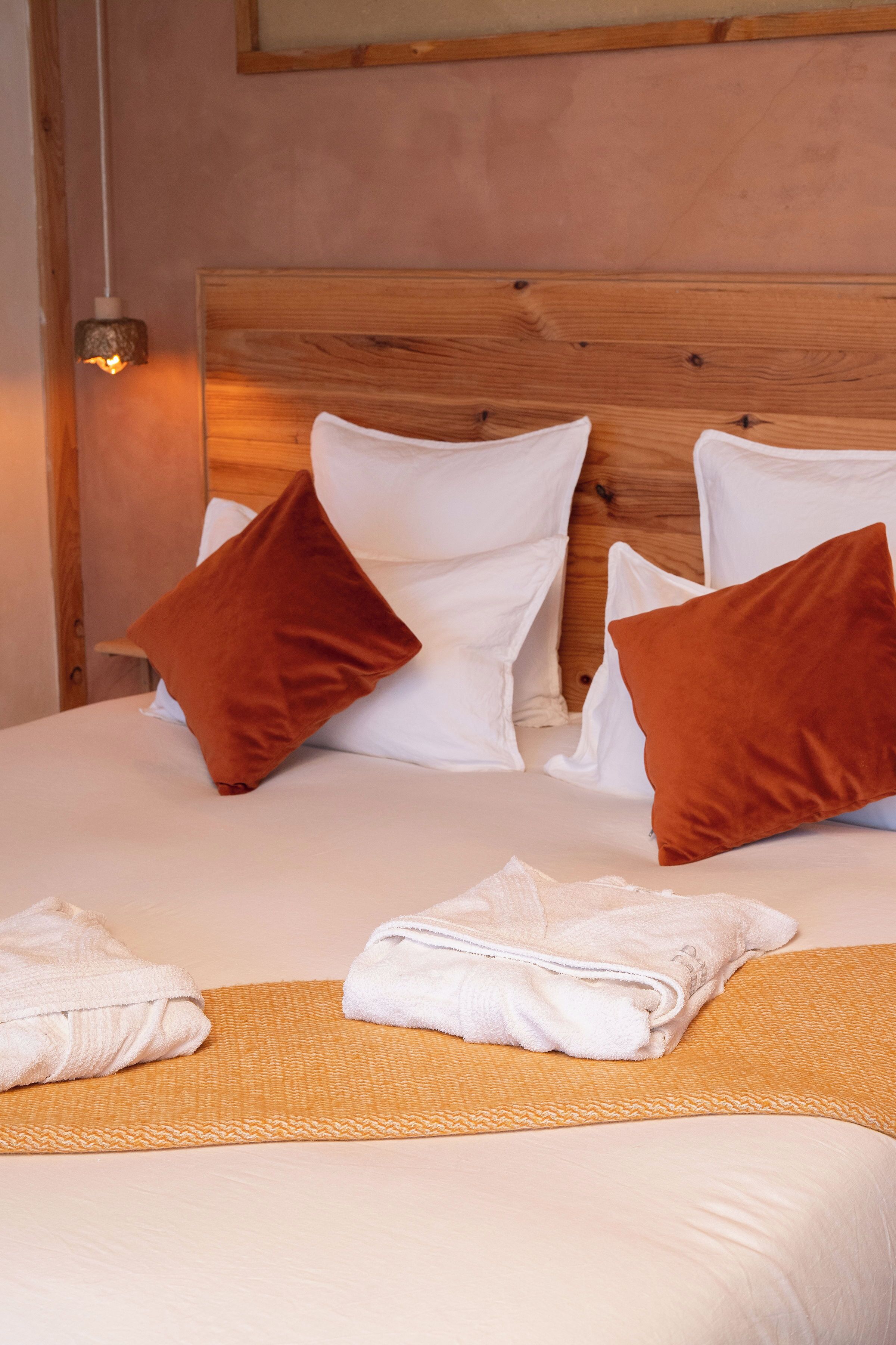 A neatly made bed with white and brown pillows, a folded towel, and a wooden headboard.