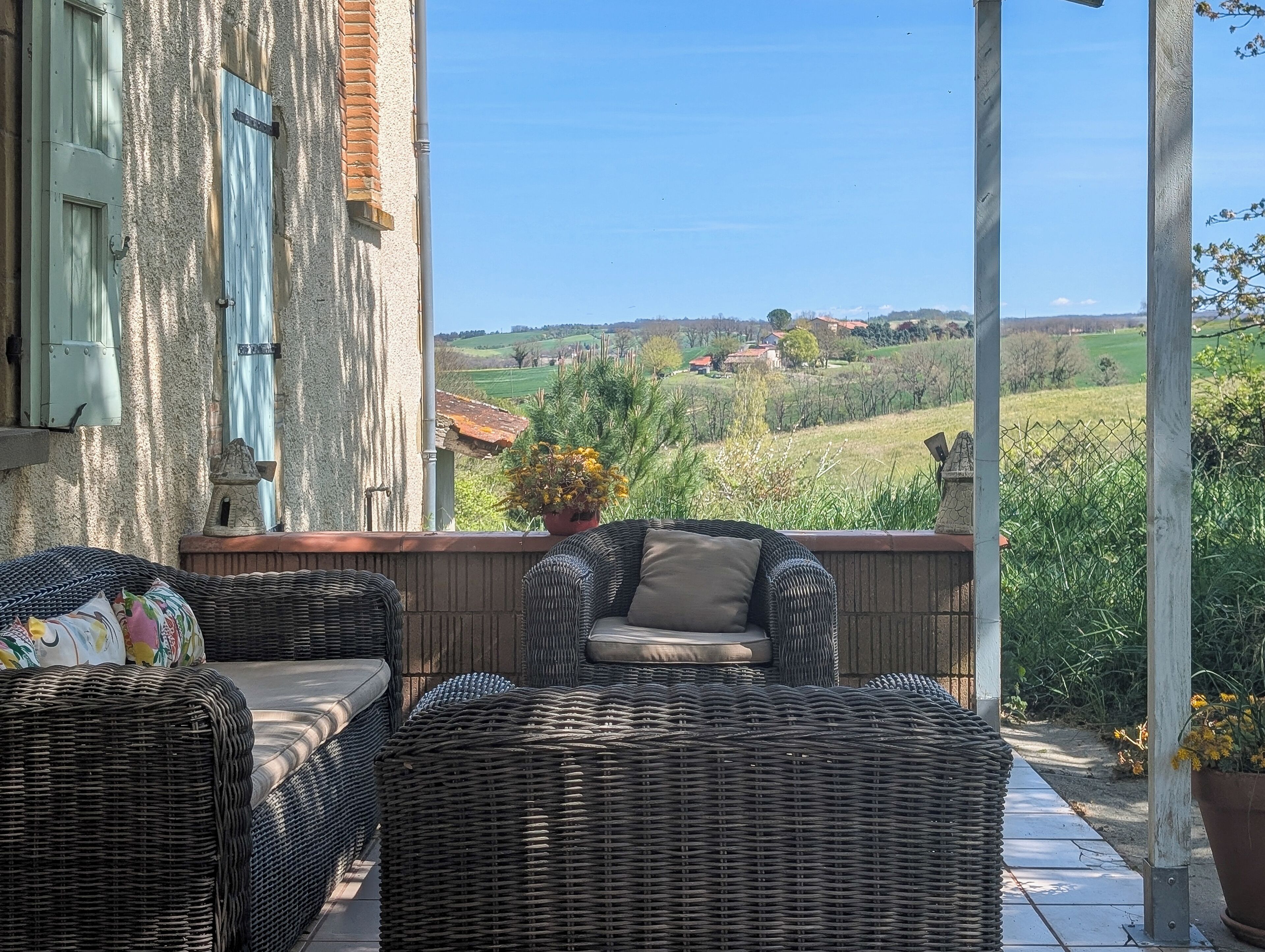 Ein Balkon mit Korbmöbeln, Blick auf eine ländliche Landschaft und ein Gebäude mit Steinverkleidung.