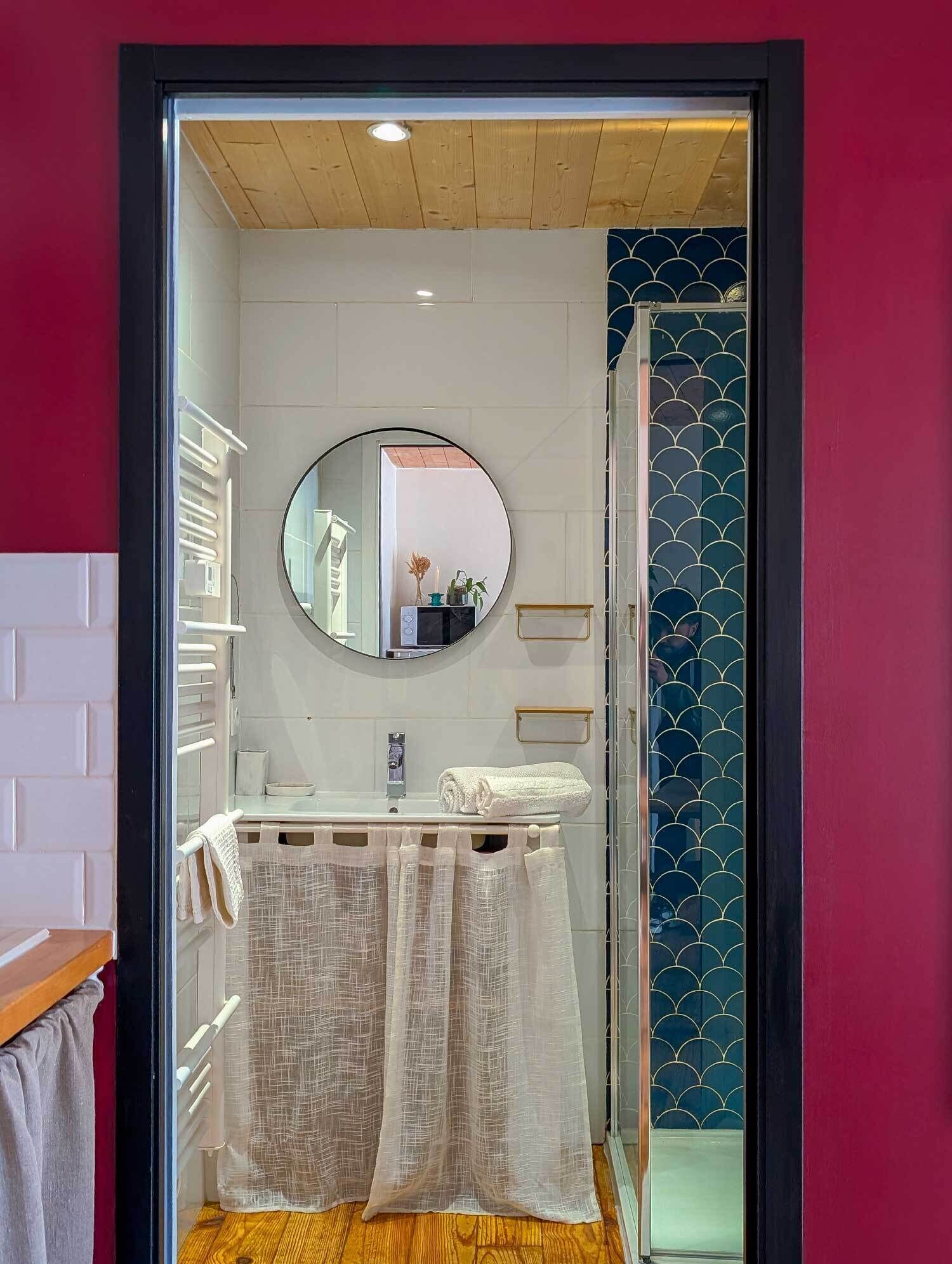 A bathroom with a wooden ceiling, a round mirror, a white sink, and a towel rack.