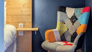 Una stanza con una parete in legno, una sedia con un cuscino patchwork, un quadro di fiori e una lampada da comodino.