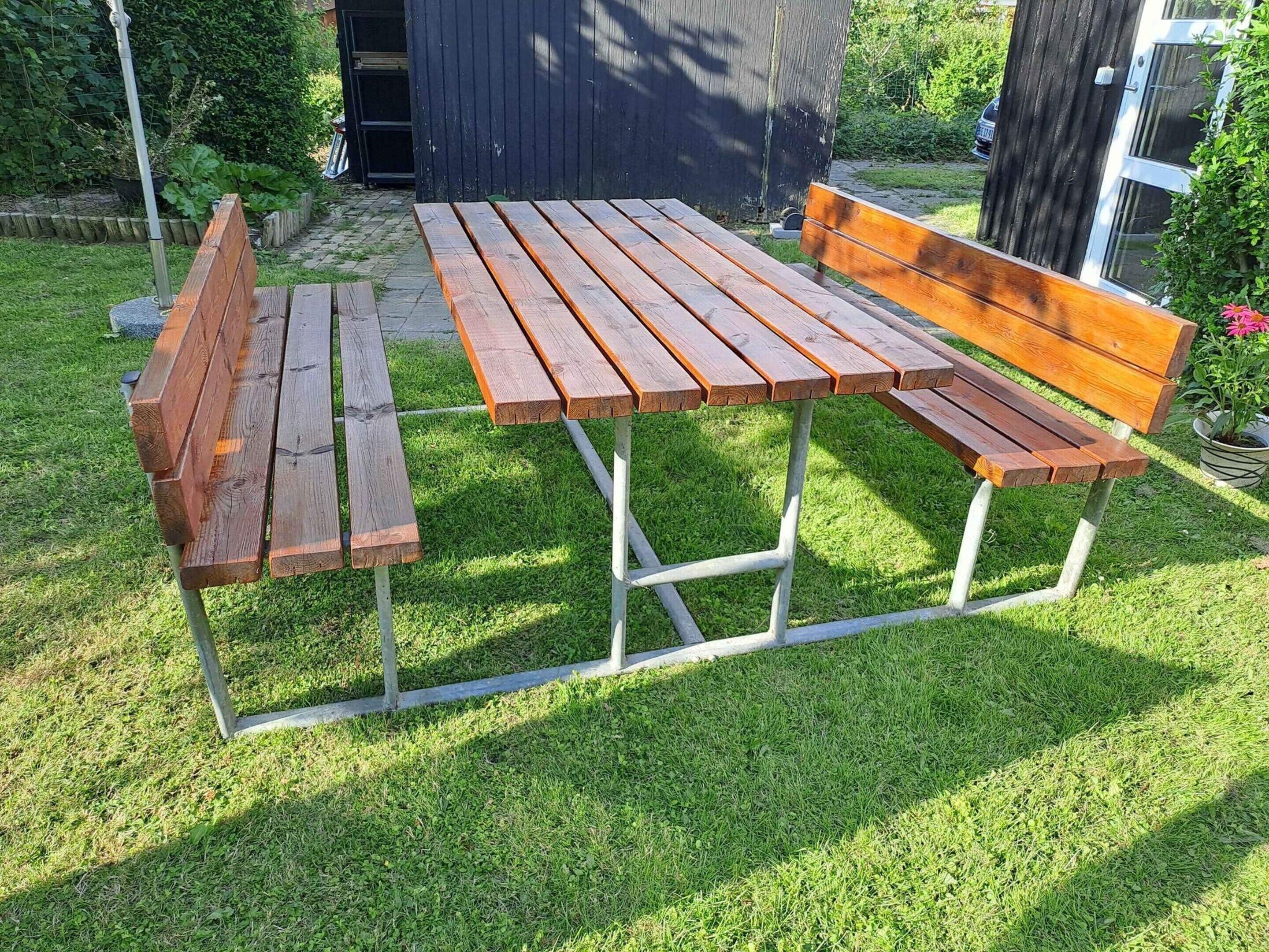 Ein Holztisch mit Bänken, auf einer grünen Rasenfläche platziert.