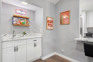 A modern kitchen with white cabinetry, a marble countertop, and a sink. There are framed pictures on the wall, including one that says 'GAME ROOM.' - 3BR by Kalahari, near UT for game days: game room, fenced yard, fire pit, pets (Round Rock)