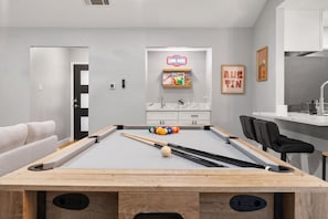 A modern pool table with a pool cue and balls, a sofa, a gaming area with a neon sign, and a framed picture. - 3BR by Kalahari, near UT for game days: game room, fenced yard, fire pit, pets (Round Rock)