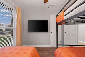 A room with two beds, a TV mounted on the wall, and a door. - 3BR by Kalahari, near UT for game days: game room, fenced yard, fire pit, pets (Round Rock)