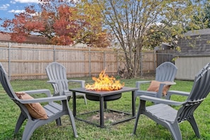 A backyard with a fire pit table surrounded by Adirondack chairs with cushions. - 3BR by Kalahari, near UT for game days: game room, fenced yard, fire pit, pets (Round Rock)