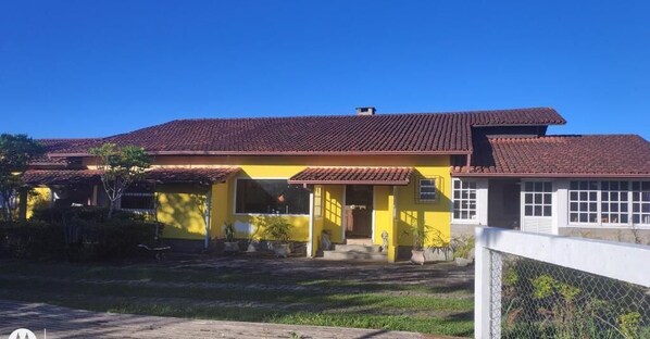 Un edificio amarillo con techo de tejas rojas, un porche cubierto y un patio cercado.