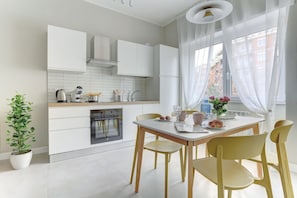 Moderni keittiö, jossa on valkoiset kaapit, sisäänrakennettu uuni sekä ruokailutila, jossa on pöytä ja tuolit.