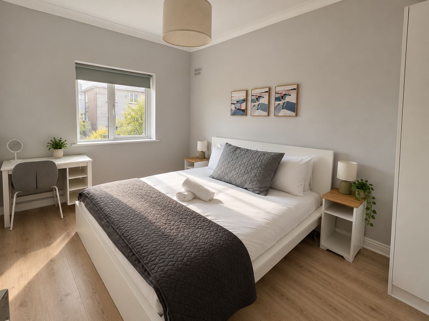 Een slaapkamer met een bed, nachtkastjes, een bureau, een stoel, een raam en kunst aan de muur.