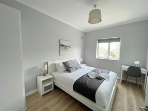 A bedroom with a bed, bedside tables, a desk, and a window.