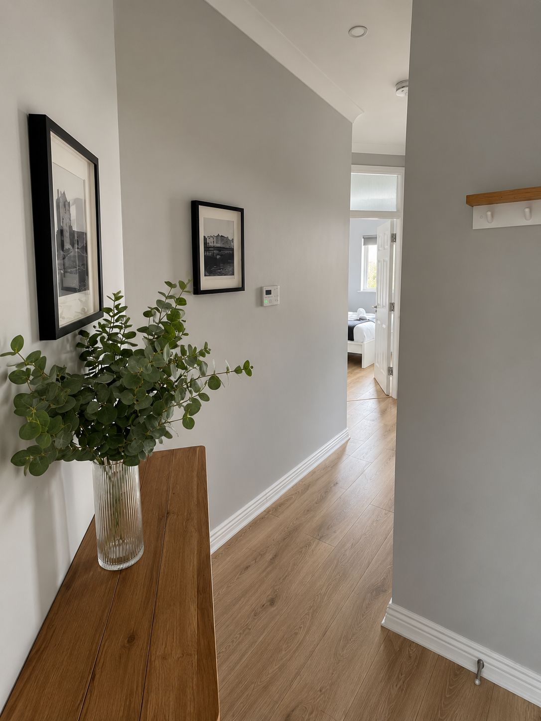 A hallway with a wooden bench, a potted plant, and two framed pictures on the wall.