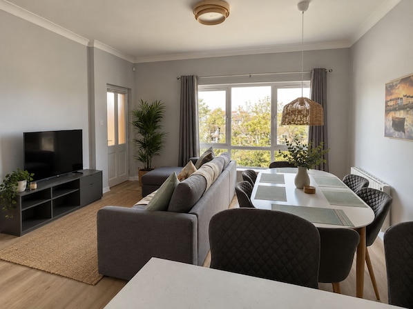 Un salon moderne comprenant un canapé, un téléviseur, une table à manger, des chaises et une vue sur l’extérieur.