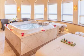 Une salle de spa équipée d’un grand bain à remous, d’une table de massage et d’un espace détente avec des fauteuils.