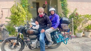 Two people on a motorcycle parked in front of a building with potted plants and a clear entrance. - Sia Taj Hotel Agra Nearest Taj Mahal (Agra)
