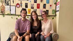 Three people sitting on a bench with a wall decorated with various posters and a clock. - Sia Taj Hotel Agra Nearest Taj Mahal (Agra)