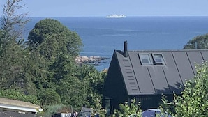 Rannikonäkymä, jossa on talo, puita ja kauempana näkyvä laiva.