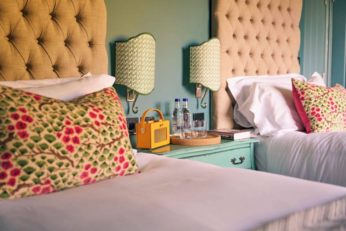 A bed with floral pillows, a bedside table with a radio, and wall-mounted lamps.
