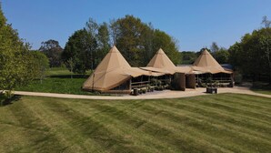 Un terrain de camping comprenant trois tentes coniques, un espace central aménagé avec des tables et des chaises, et une pelouse bien entretenue.