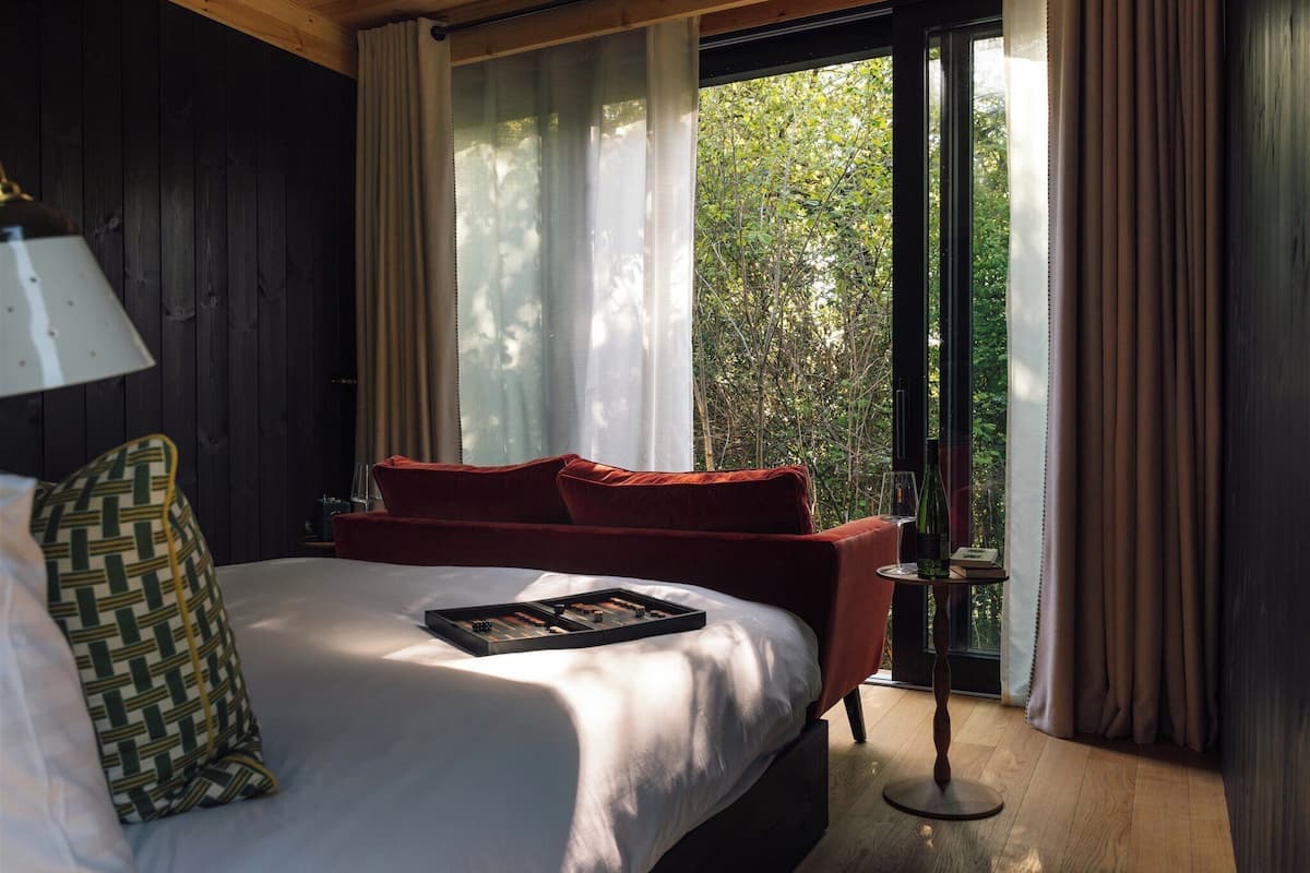A bedroom with a bed, a red sofa, a lamp, and a window with curtains.