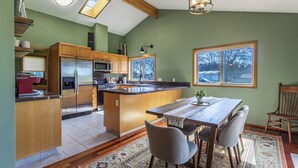 A kitchen with a central island, wooden cabinets, a refrigerator, and a dining area with a table and chairs.