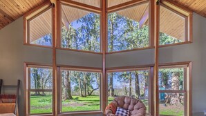 A room with large windows, a wooden ceiling, and a chair with a cushion.