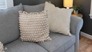 A grey sofa with two textured pillows, a world map on the wall, and a lamp on a side table. - Low Tide - Heart of Hampton Beach! (Hampton)