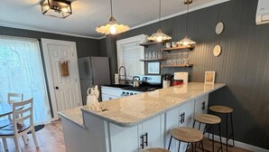 Une cuisine dotée d’un îlot central, de tabourets de bar, de luminaires suspendus et d’un réfrigérateur.