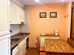 Une cuisine compacte avec des meubles blancs, une cuisinière et un évier. On y trouve une petite table à manger avec des chaises.