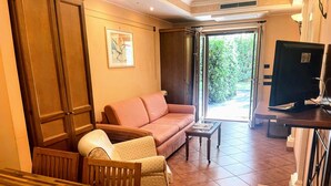 Una habitación con una mesa de comedor de madera, un sofá, un televisor y un ventanal corredero que da a un jardín.