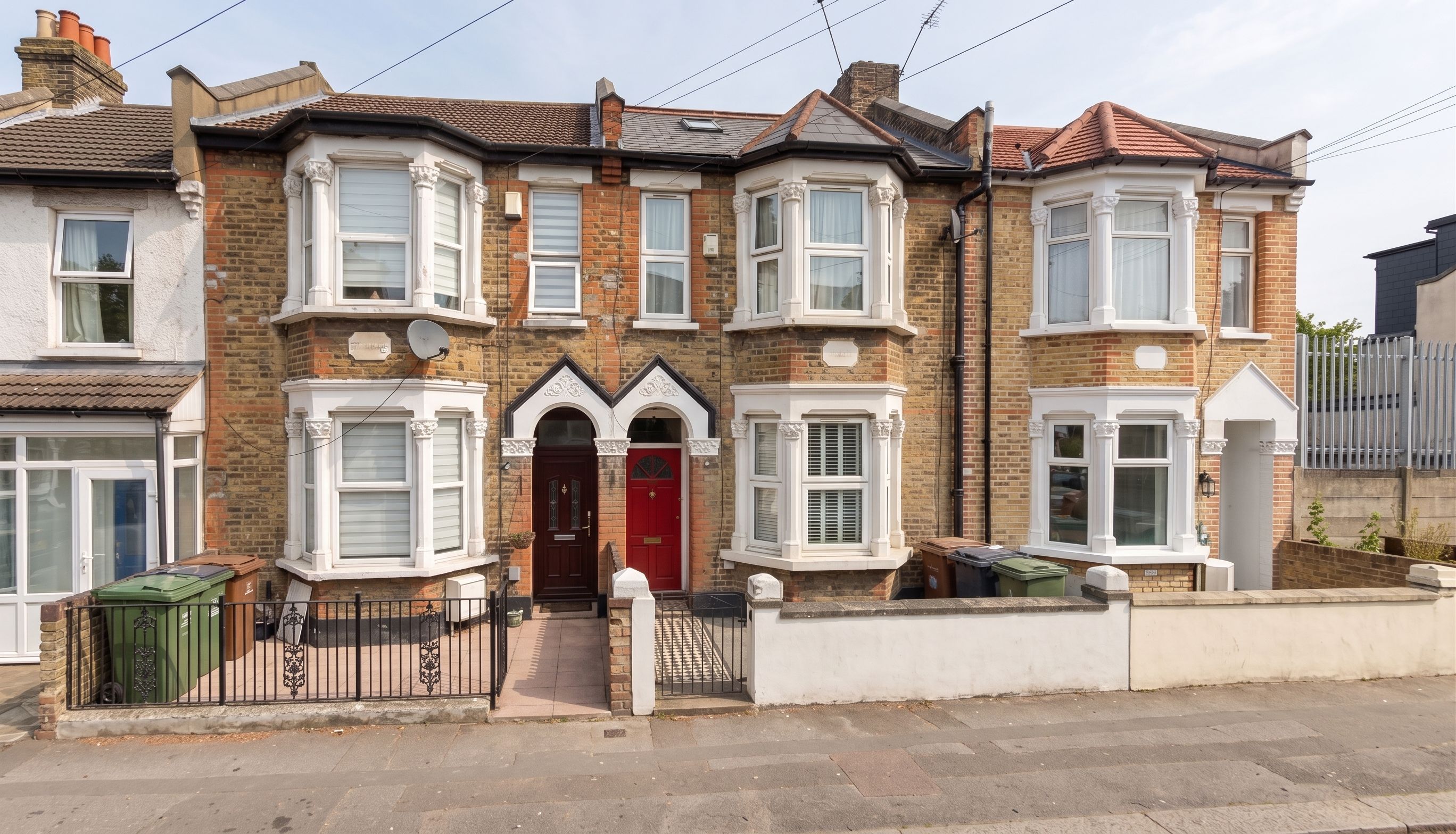A two-story terraced house with a red front door, bay windows, and a brick facade.