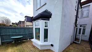 A house with a white exterior, a wooden deck, and a small window with a black frame. - Modern 2BDR Home with Garden in Walthamstow (Greater London)