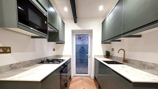 A modern kitchen with a central island, double overhead cabinets, a built-in microwave, and a herringbone wood floor. - Modern 2BDR Home with Garden in Walthamstow (Greater London)