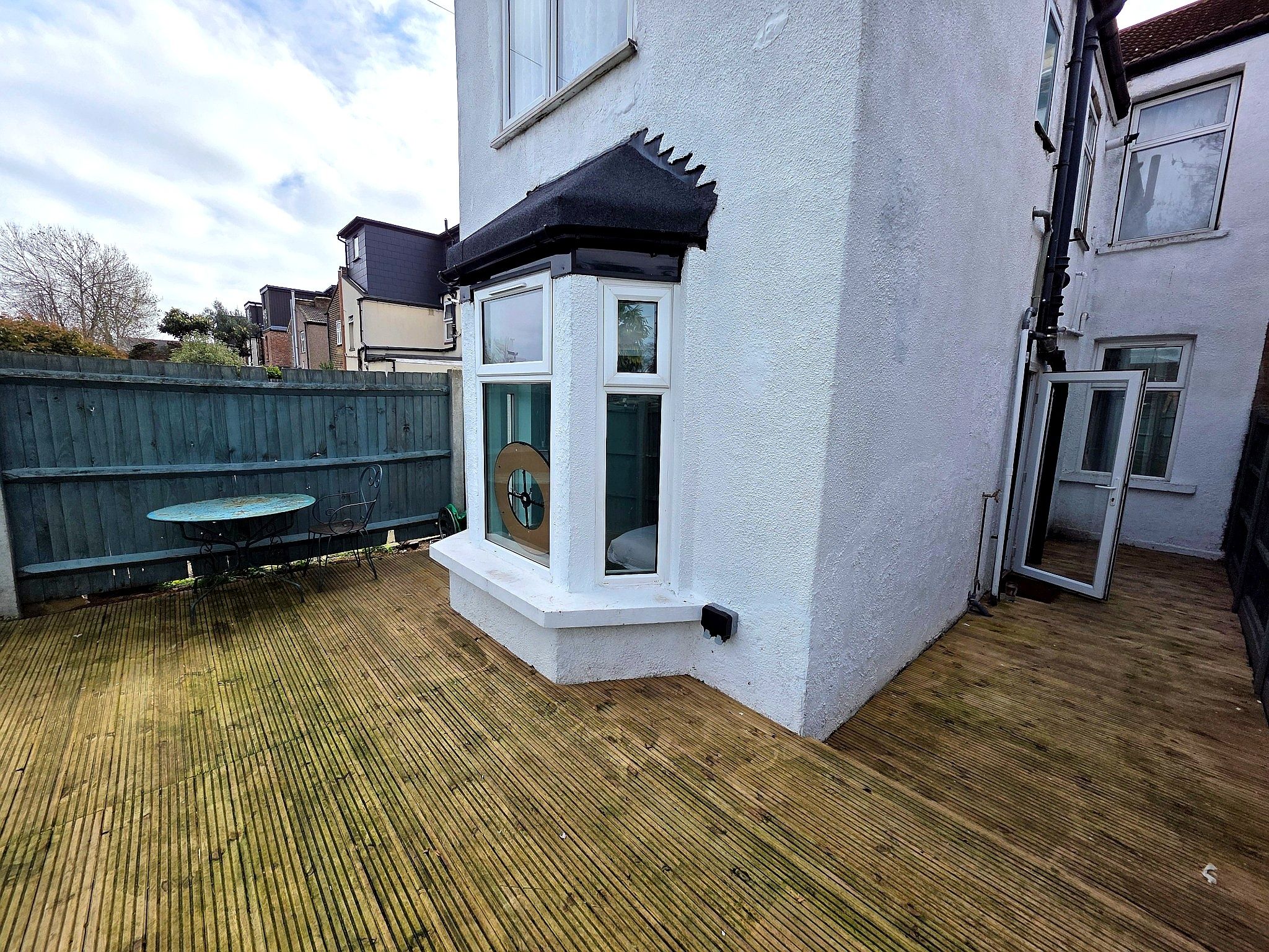 A residential property with a wooden deck, a small outdoor seating area, and a white exterior wall.