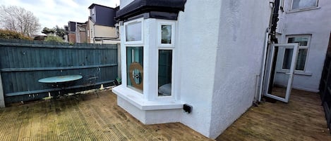 A residential property with a wooden deck, a small outdoor seating area, and a white exterior wall.