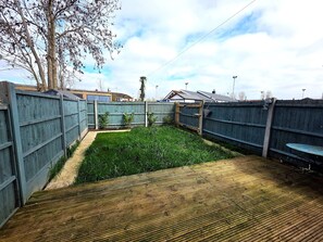 A fenced backyard with a grassy area and a wooden deck. - Modern 2BDR Home with Garden in Walthamstow (Greater London)
