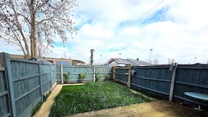 A fenced backyard with a grassy area and a wooden deck. - Modern 2BDR Home with Garden in Walthamstow (Greater London)