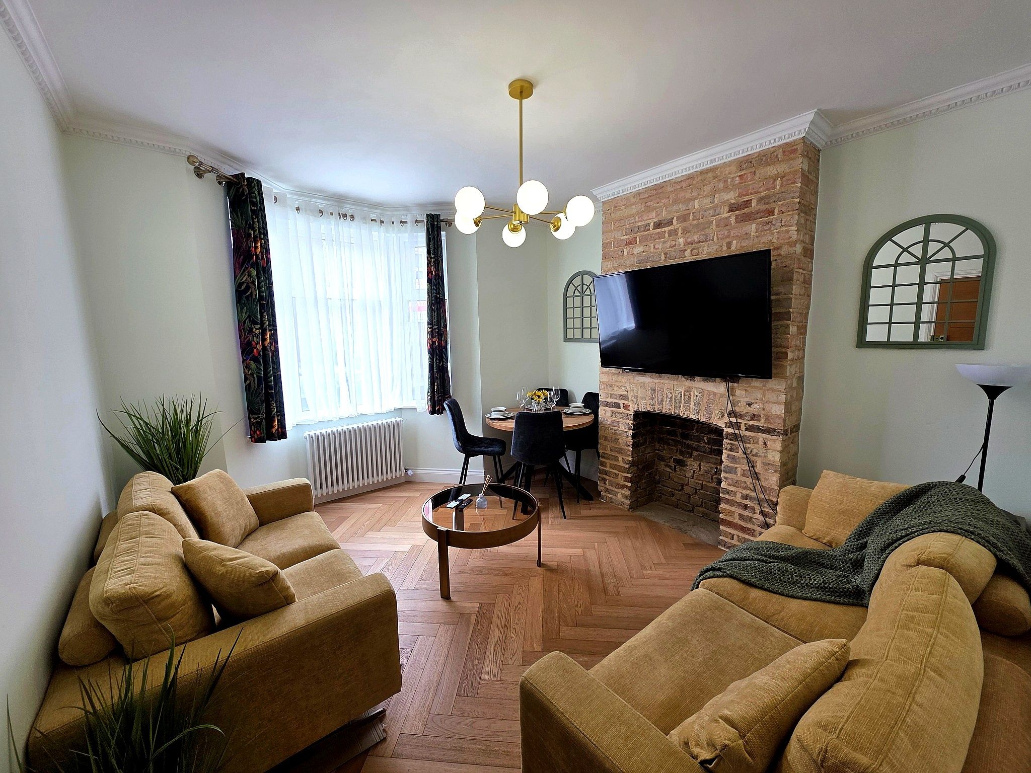 A living room with a brick fireplace, a flat-screen TV, and a dining area with a table and chairs.