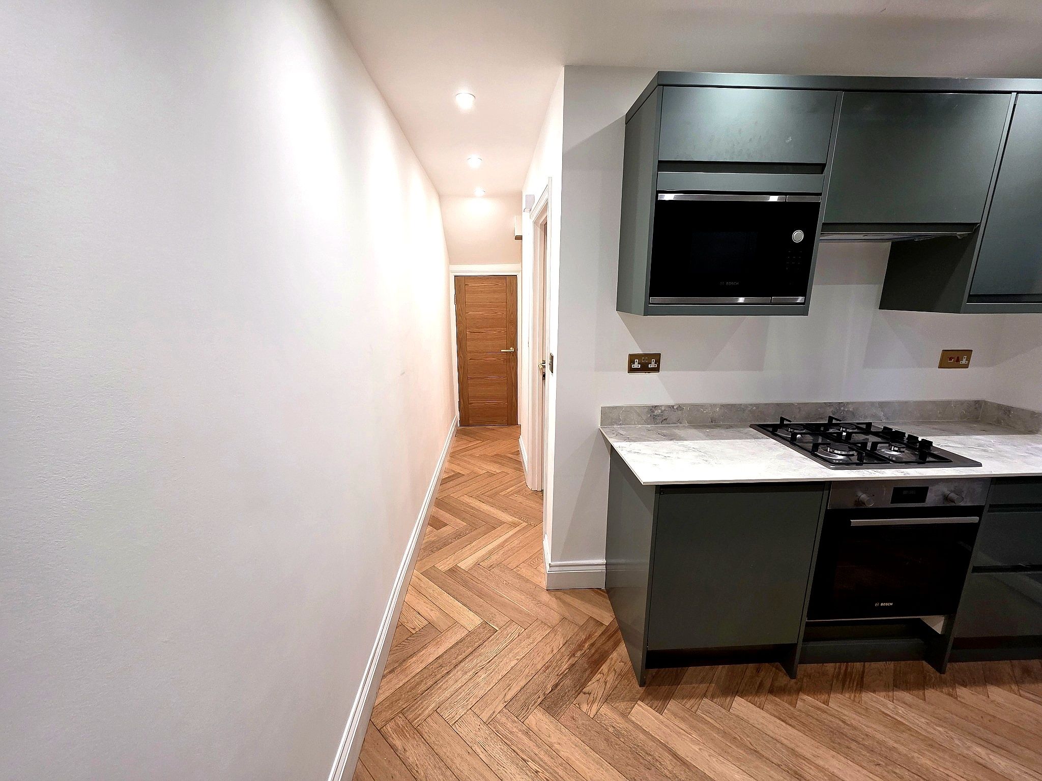 A modern kitchen with a herringbone wood floor, a central island with a gas stove, and built-in appliances including a Bosch microwave and oven.