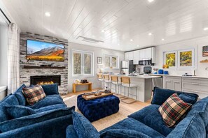 Ein modernes Wohnzimmer mit Kamin, eine Küche mit weißen Schränken und ein Essbereich mit Barhocker.