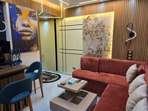 A modern living room with a red sofa, a coffee table, and a blue chair. There is a painting on the wall and a textured wall feature.