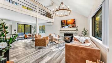 A spacious living room with a fireplace, a large window, and a high ceiling.