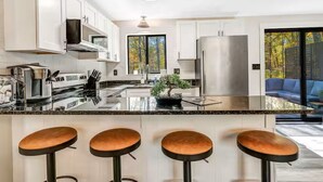 A modern kitchen with white cabinets, stainless steel appliances, a central island with stools, and a view of the outdoors. - Bushkill Bliss w/ Hot tub near Falls & Shawnee (East Stroudsburg)