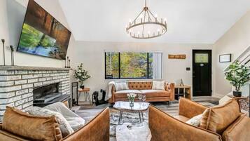 A living room with a fireplace, leather sofas, a chandelier, and a large window with a view of trees.
