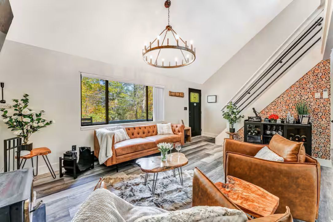 A spacious living room with a large window, a leather sofa, a coffee table, and a chandelier.