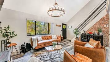A spacious living room with a large window, a leather sofa, a coffee table, and a chandelier.